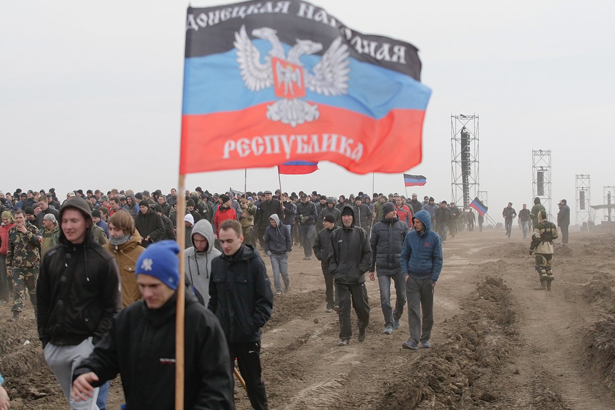 Местные жители с флагом ДНР в руках идут колонной во время мобилизационных сборов на Торезском полигоне недалеко от контролируемого пророссийскими повстанцами города Шахтерск Донецкой области, Украина, 6 апреля 2017. Фото: Alexander Ermochenko / EPA-EFE